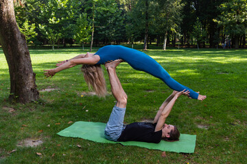 Boy and girl doing acro yoga outdoors in summer in public park