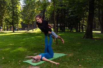 Boy and girl doing acro yoga outdoors in summer in public park