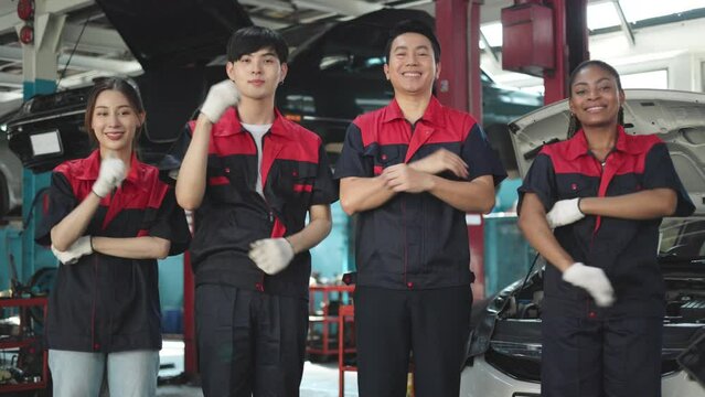 Engineer team checking under car condition on lifter in garage.Young auto mechanic in uniform is looking at camera and smiling examining car.