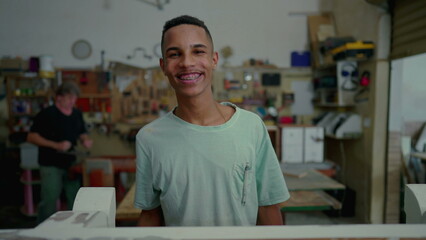 Fototapeta premium Portrait of a happy black Brazilian employee of carpentry workshop, local small business occupation. Young apprentice looking at camera smiling