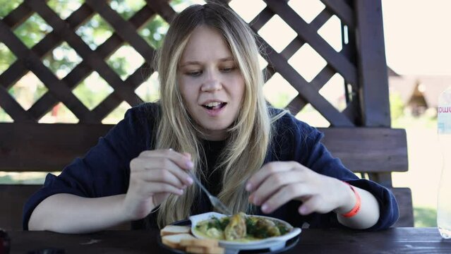 beautiful blonde girl eats a dish of snails with cheese, looks at the camera and laughs. lunch in nature