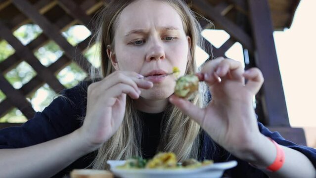 the girl is concentrating on pulling the snail out of the shell and chewing. a woman eats a dish of snails with cheese