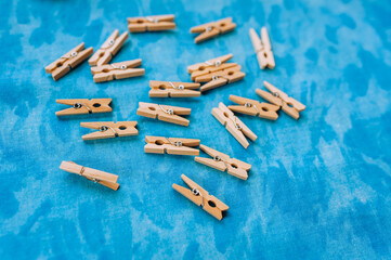 A lot of small wooden clothespins lying on a blue fabric background. Close-up photography, household, background.