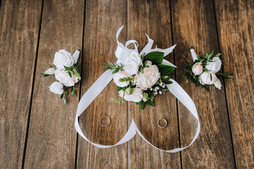 Obraz na płótnie Canvas A bouquet of flowers with a ribbon in the form of a heart, a boutonniere, golden rings of the newlyweds lie on a wooden background. Wedding photography, top view.