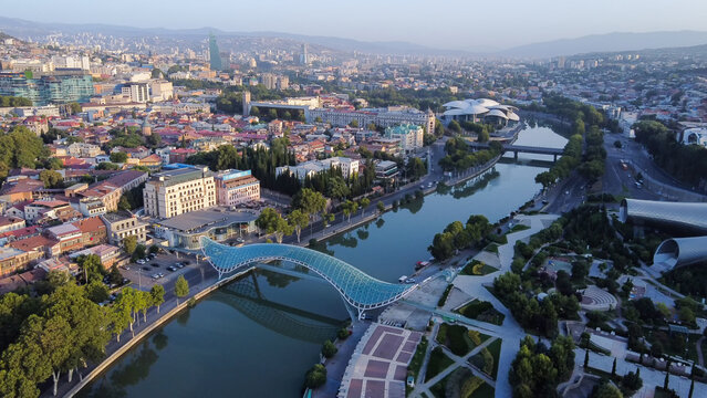 Sunrise in  Georgian capital -Tbilisi , pedstrian bridge of  Peace over Kura river and  cityscape with President building in distance