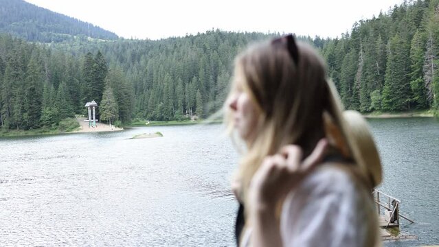 beautiful blonde girl wears a straw hat with a black ribbon and looks at the lake in the mountains. a woman near Lake Synevir