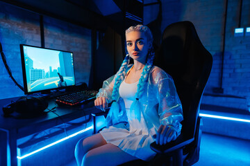 Young female blogger, gamer plays games on computer. Neon computer club.