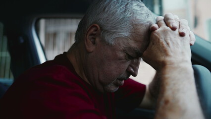 Regretful senior man feeling shame and guilt, remembering trauma from the past, struggling alone inside parked car leaning forward holding into steering wheel