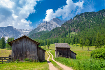 Path into meadow between wooden huts in front of dolomites mountains, Trentino, Fischleintal