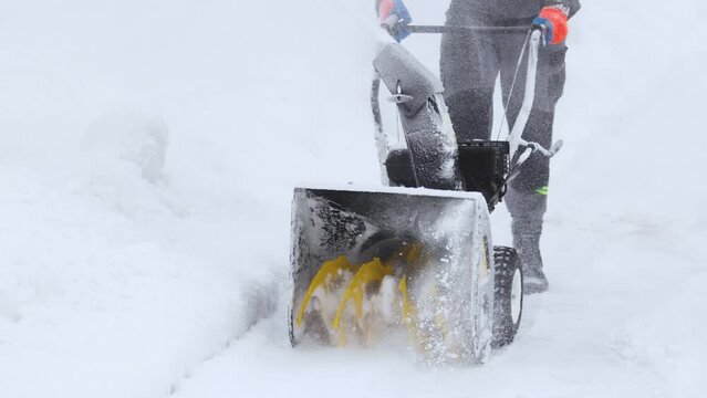 Process of removing snow with portable blower machine, worker dressed in overall workwear with gas snow blower removal on the street during snowy winter after massive snowfall, slow motion