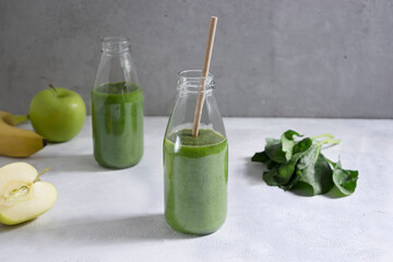 Green smoothie from banana, apple, spinach and kiwi in glass bottles on a light gray background. Healthy green smoothie.