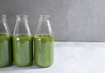 Green smoothie from banana, apple, spinach and kiwi in glass bottles on a light gray background. Healthy green smoothie.