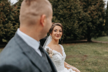 Fototapeta premium Stylish bride and groom tenderly embrace and kiss. Beautiful bride with modern bouquet embracing stylish groom in autumn park. Sensual romantic moment. Wedding. Stylish and beautiful.