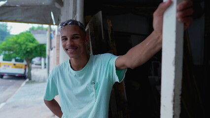 One happy black Brazilian young man standing by sidewalk street smiling at camera. Authentic real life from South America portrait with friendly expression