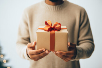 Close-up view of man's hands holding gift box wrapped with paper with red ribbon.