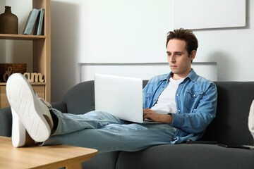 Fototapeta premium Male freelancer working with laptop on sofa at home