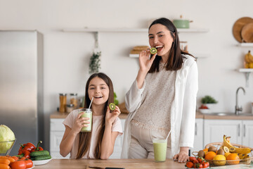 Little girl with her pregnant mother drinking green smoothie in kitchen