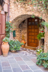 Fototapeta na wymiar Historic house entrance in a small Italian town, hidden in a brick archway. The entrance is decorated with planters and green plants and invites you into a pleasantly cool apartment.