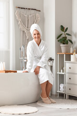 Mature woman with towel sitting in bathroom