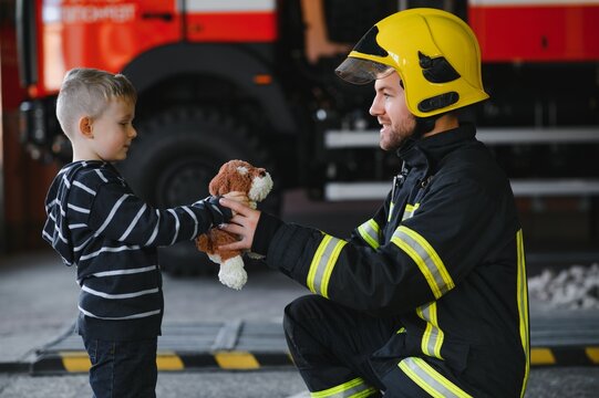 Dirty firefighter in uniform holding little saved boy standing on black background.
