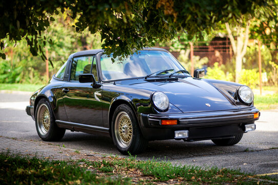 Brno, Czech Republic - August 22, 2023: Old black sports car Porsche 911 from the eighties is parked on the street by a tree.