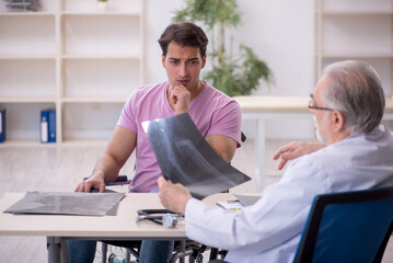 Fototapeta premium Young man in wheelchair visiting old doctor radiologist
