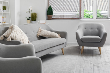 Interior of light living room with cozy grey sofa and armchairs