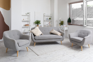 Interior of light living room with cozy grey sofa and armchairs