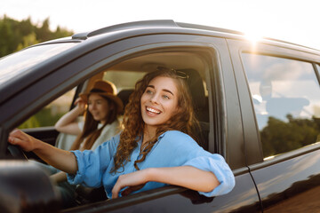 Two women travelers travel by car, have fun. Beautiful female friends in the car enjoy a car trip together. Travel, tourism.