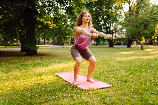 Athletic woman doing exercises with dumbbells outdoors on a sunny day. Sports concept. Active lifestyle.