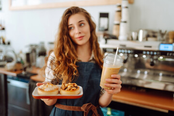 Young coffee shop worker holding takeaway drinks and desserts. Business concept, food to go, small business.