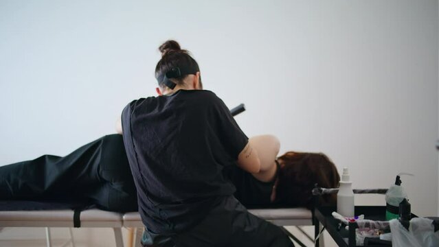 Back view artist tattooing at salon. Serious woman taking ink working at studio