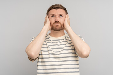 Tensed confused desperated man clutched cheeks looking up on grey background. Advertisement banner, poster for sale, marketing concept. Frustrated guy feels negative emotions has problems, troubles.