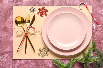 Festive table setting with fir tree branches, plates, cutlery and decorations on pink background