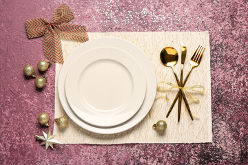 Festive table setting with cutlery, Christmas balls and bow decorations on pink background