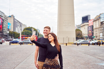 portrait young caucasian heterosexual couple taking selfie happy at the Obelisk in Buenos Aires
