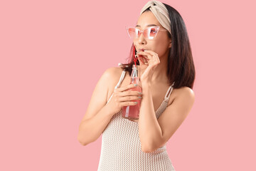 Naklejka premium Beautiful Asian woman in swimsuit and with drink on pink background