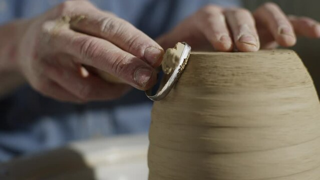 A close-up of the ceramicist's hands cutting off excess clay from the product. The art of ceramics, the work of a master in a workshop. High quality 4k footage