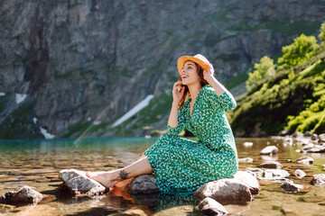 Young woman in a dress and hat enjoys the scenery on a high mountain lake. Romantic tourist posing against the background of mountain landscapes.