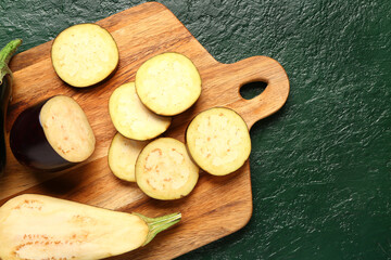 Wooden board with fresh cut eggplant on green background