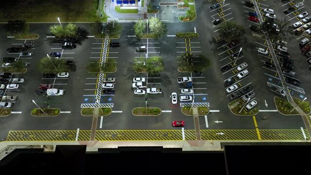 Top view of many cars parked at night on brightly illuminated parking lot in front of a grocery shopping mall. Concept of consumerism and market economy
