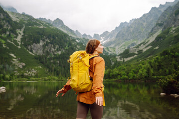 Travel Slovakia, Europe. Tourist with a yellow backpack stands against the backdrop of an alpine lake. The concept of freedom, tourism, hiking, nature