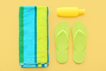 Pair of green flip flops with blanket and sunscreen cream on yellow background