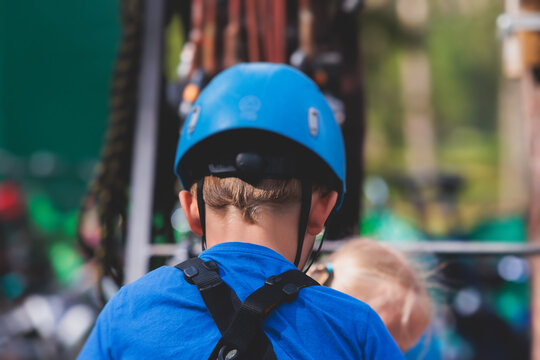 View of high ropes course, kids of climbing in amusement acitivity rope park, passing obstacles and zip line on heights, children teenagers in equipment gear between the trees on heights, summer day