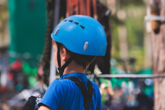 View of high ropes course, kids of climbing in amusement acitivity rope park, passing obstacles and zip line on heights, children teenagers in equipment gear between the trees on heights, summer day