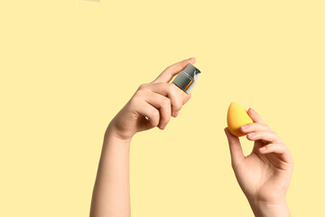 Female hands with makeup sponge and bottle of foundation on beige background
