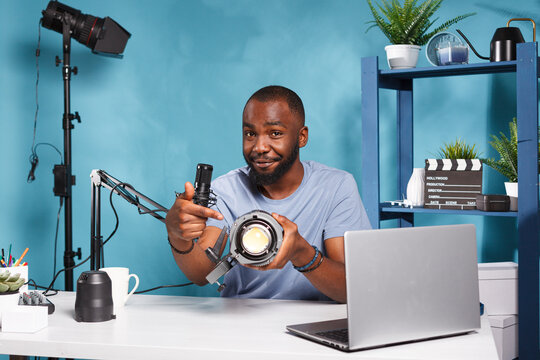 Internet influencer recommending studio lightning equipment while recording video review. Smiling african american blogger pointing at videography tool while promoting product online