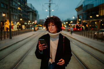 Fototapeta premium Dark haired woman standing at the train station and looking down to her phone.