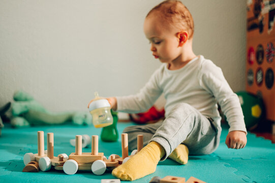 A cute little boy is playing a fun game with his baby bottle and a wooden toy at home.