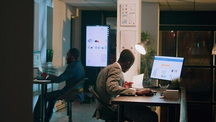 Revealing shot of employees checking company figures, postings and documents for accuracy during nighshift. Staff member working overnight, analyzing stored computerized financial information